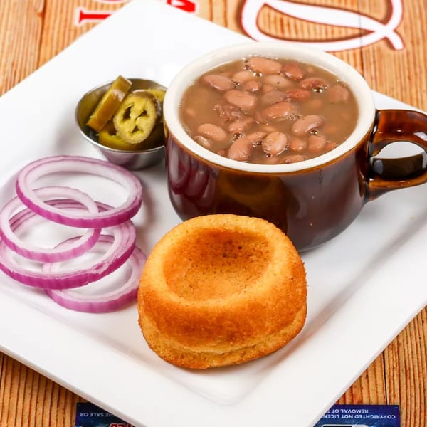 A bowl of pinto beans, a cornbread muffin, red onion slices, and pickled jalapeños on a white plate.