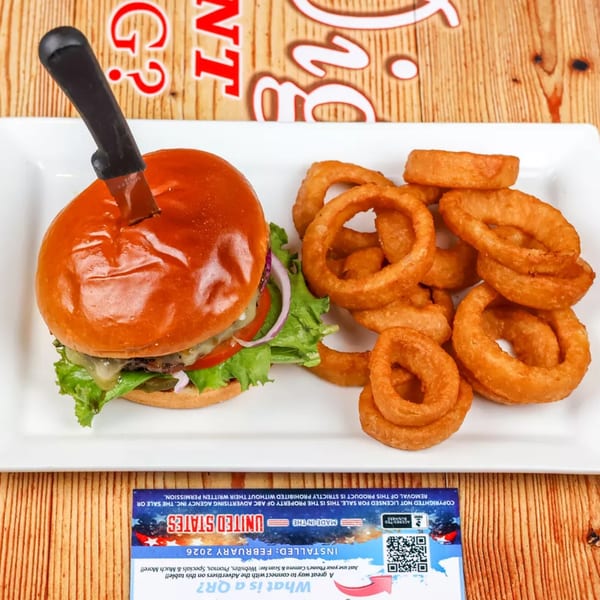 A burger with a knife in its bun, served with a side of golden onion rings.