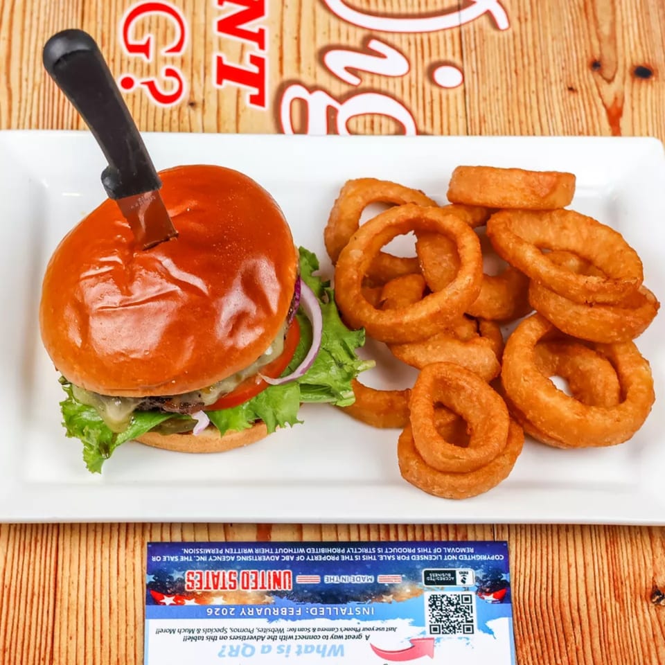 A burger with a knife in its bun, served with a side of golden onion rings.