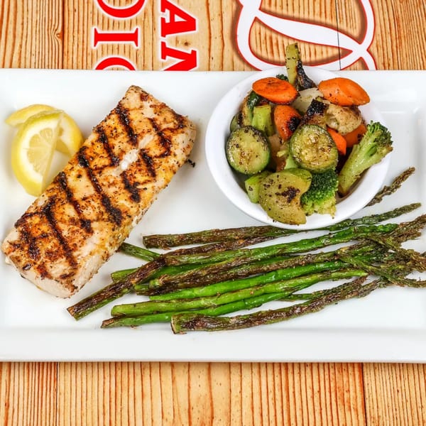 Grilled fish with lemon wedges, roasted asparagus, and a side of mixed vegetables.