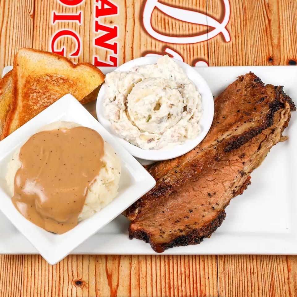 Platter with sliced brisket, mashed potatoes with gravy, potato salad, and toasted bread.