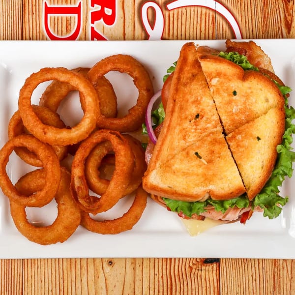 A golden-brown grilled sandwich with lettuce, cheese, and meat, served with crispy onion rings.