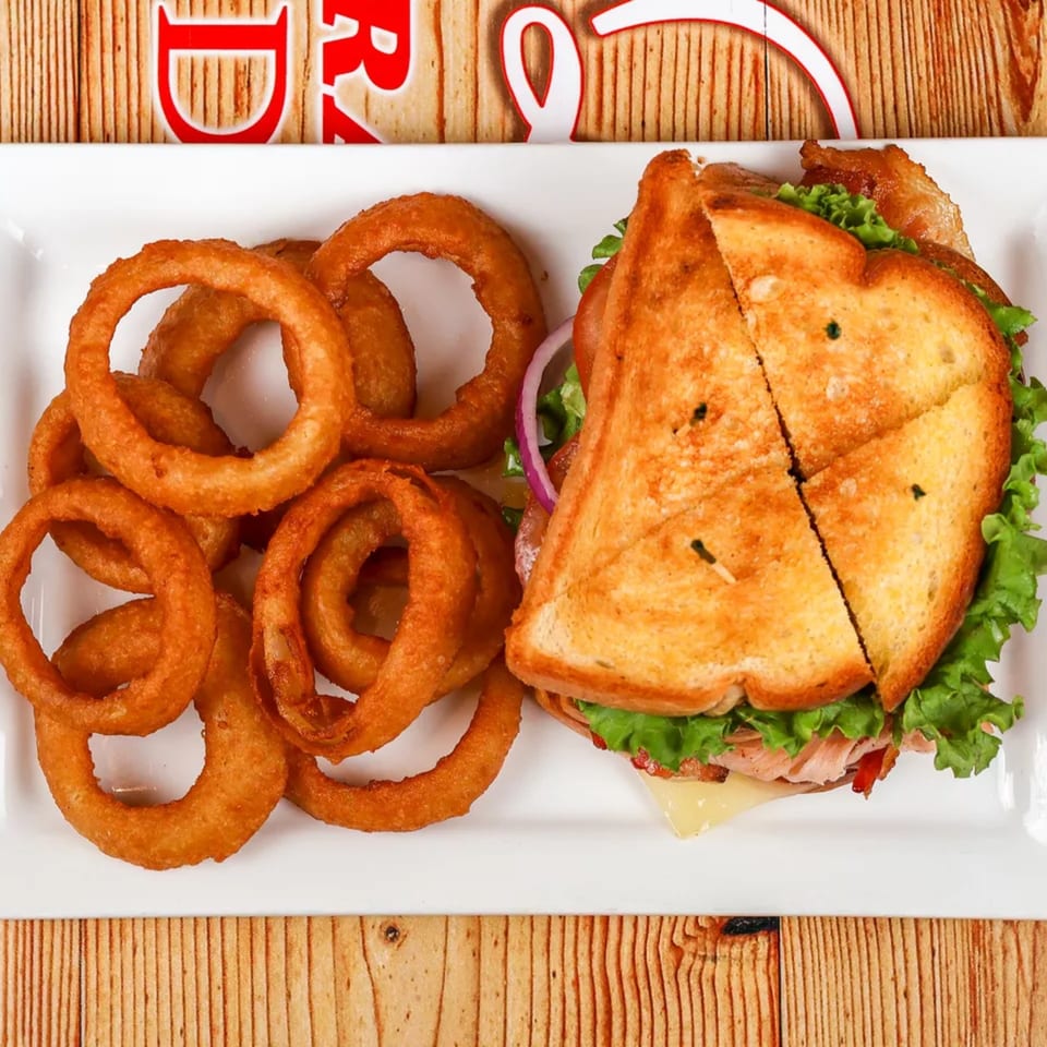 A golden-brown grilled sandwich with lettuce, cheese, and meat, served with crispy onion rings.