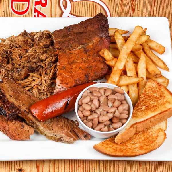 A platter of barbecue ribs, pulled pork, brisket, sausage, fries, baked beans, and toast.