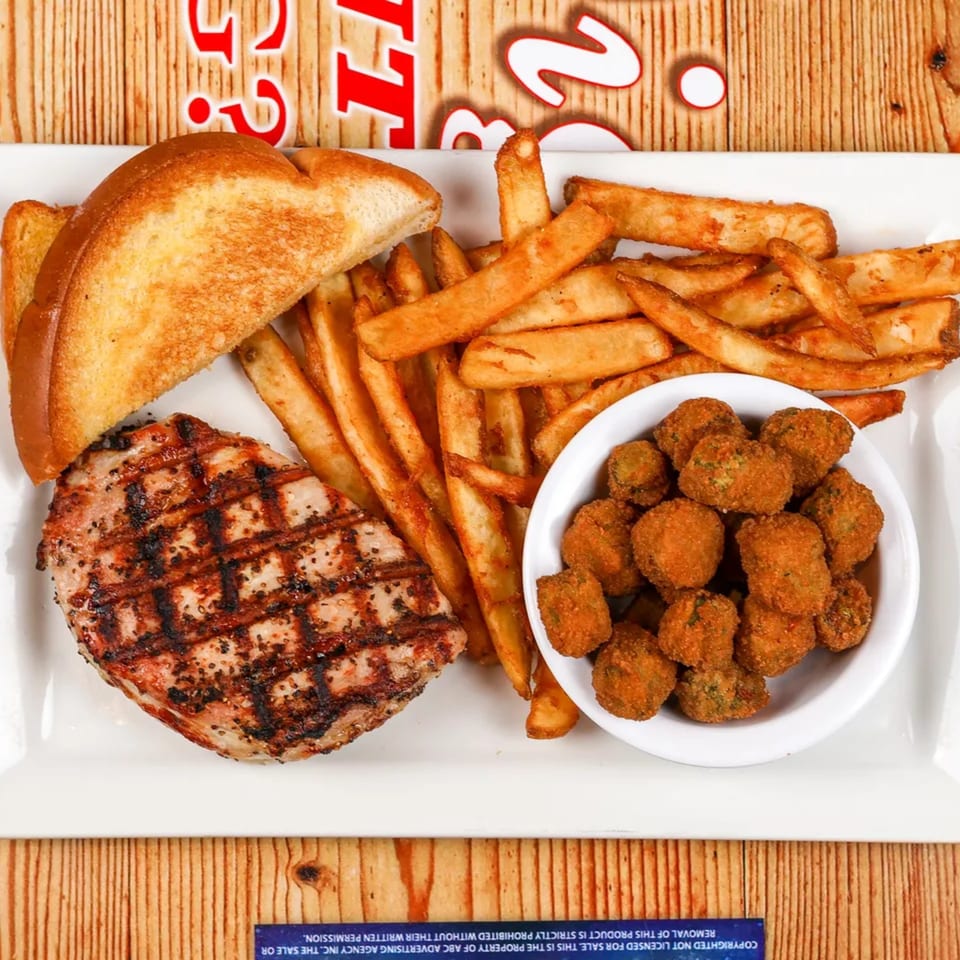 Grilled pork chop, golden fries, toasted bread, and a bowl of fried mushrooms on a white plate.