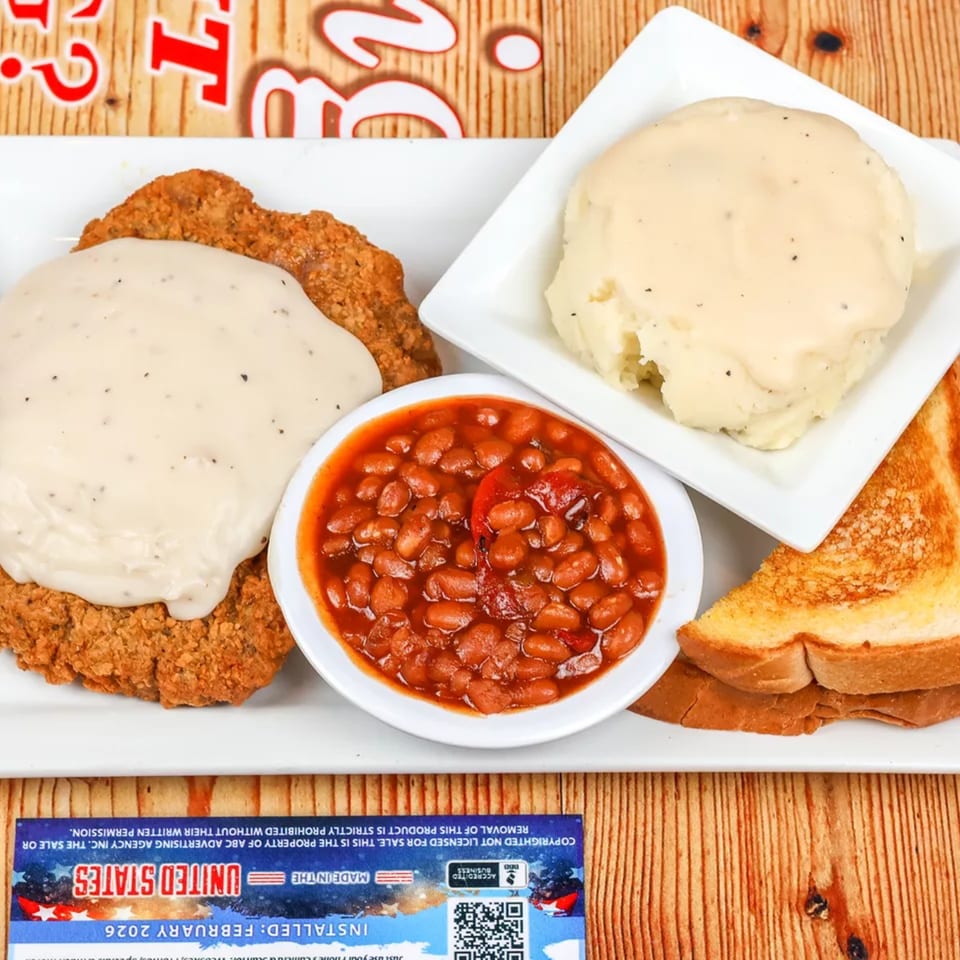 Chicken fried steak with gravy, baked beans, mashed potatoes, and Texas toast on a white plate.