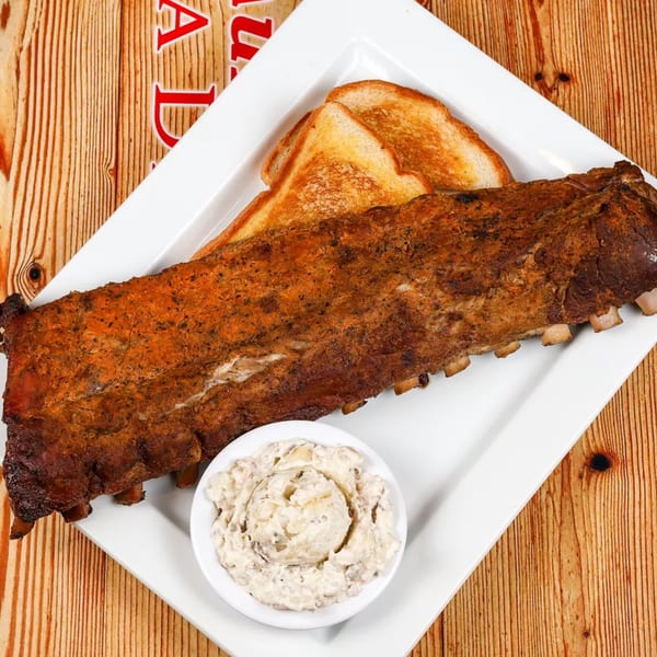 A full rack of BBQ ribs, toasted bread, and a side of creamy coleslaw on a white plate.