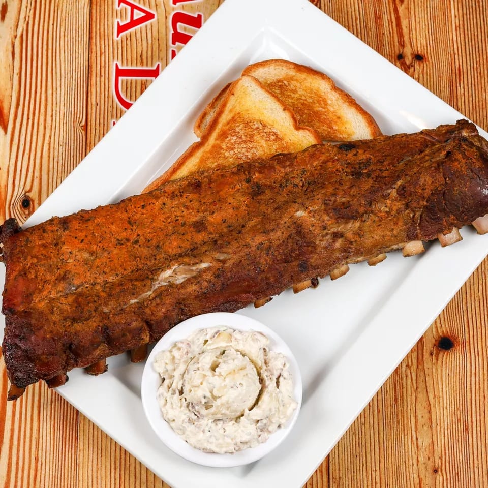A full rack of BBQ ribs, toasted bread, and a side of creamy coleslaw on a white plate.