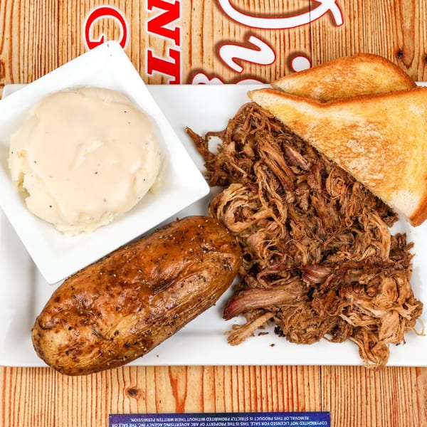 Pulled pork with toasted bread, a baked potato, and mashed potatoes on a white plate.