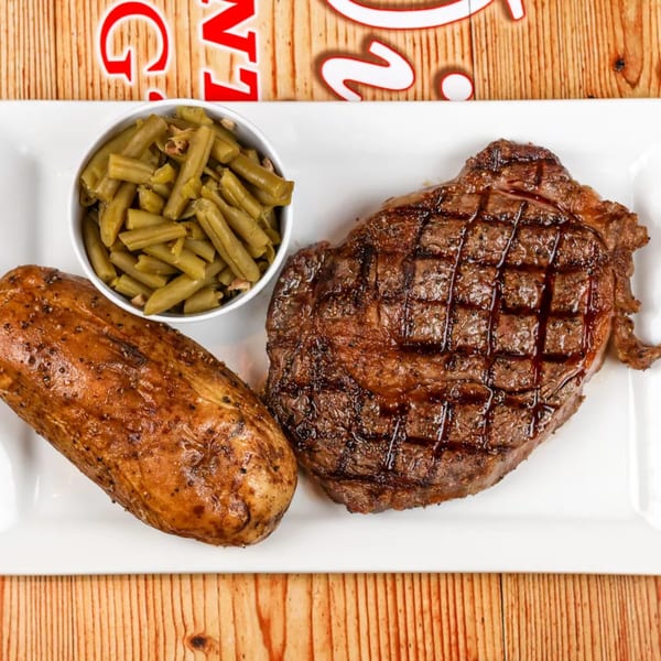 Grilled steak with grill marks, a baked potato, and a side of green beans on a white plate.